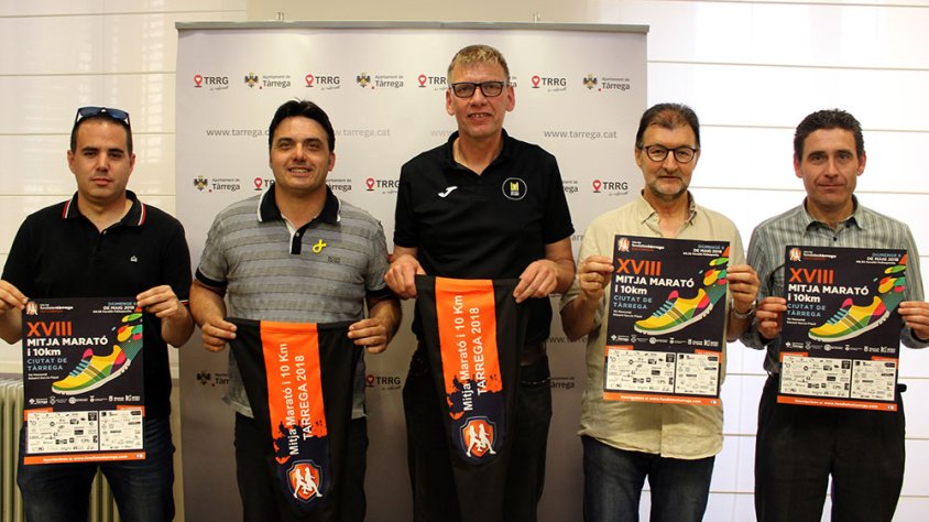 El regidor d’Esports, Jaume Folguera; el president del Club d'Atletisme 100x100 Fondistes de Tàrrega, Bart Loomans; i membres de l’entitat esportiva, amb el cartell i els obsequis de la cursa d’enguany