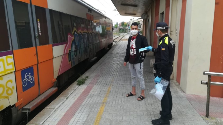 Un agent lliurant una mascareta a un usuari a l'estació de tren