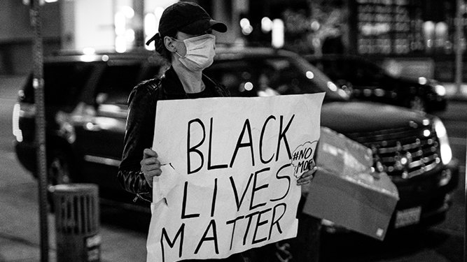 Una noia amb un cartell amb la crida '#BlackLivesMatter'