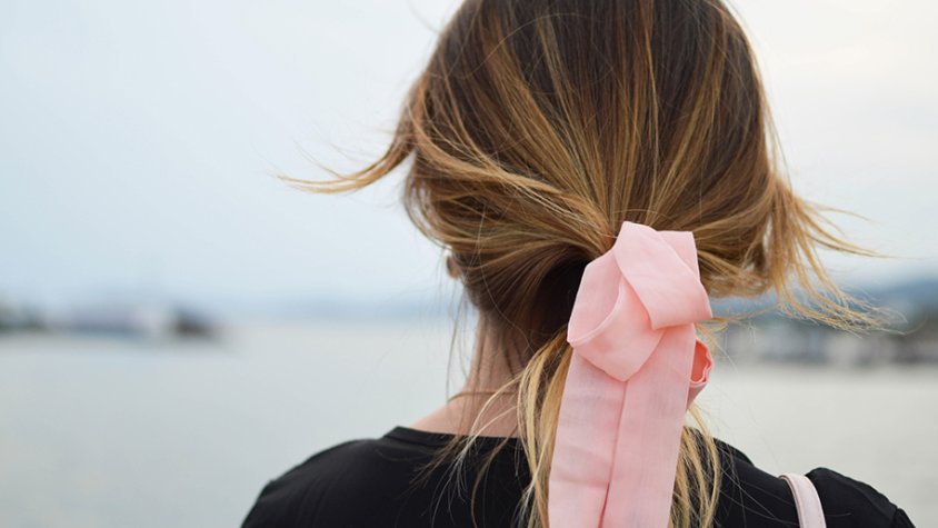 Una noia amb un llaç rosa a la cua mirant l'horitzó