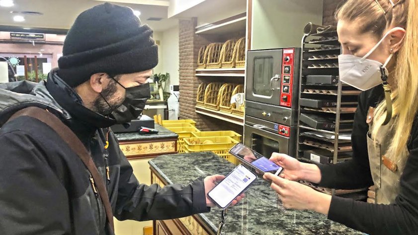 Un client d'un forn de pa de Tàrrega amb servei de cafeteria mostra el passaport Covid a la dependenta