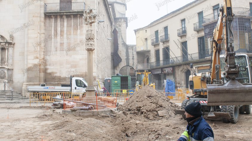Operaris treballant a la plaça Major amb la creu de terme al fons