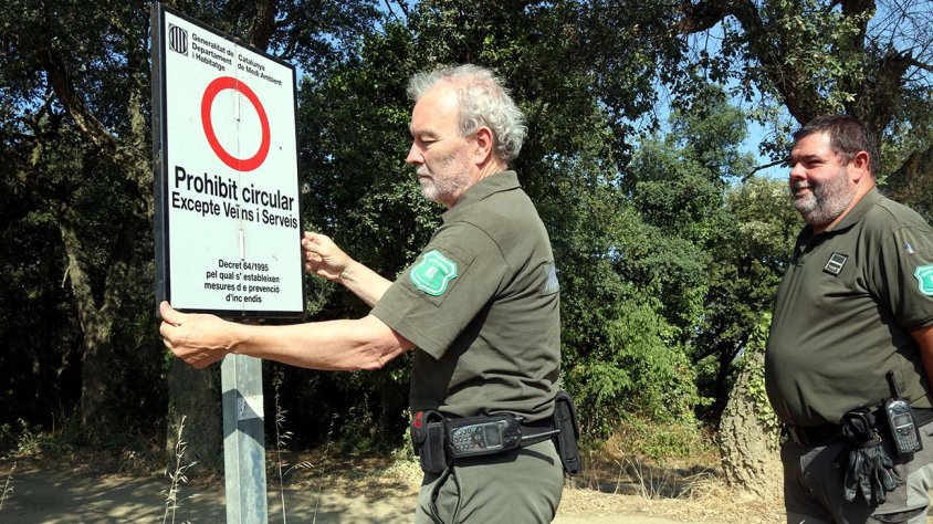 Agents Rurals desplegant un cartell que impedeix el pas al massís de les Gavarres