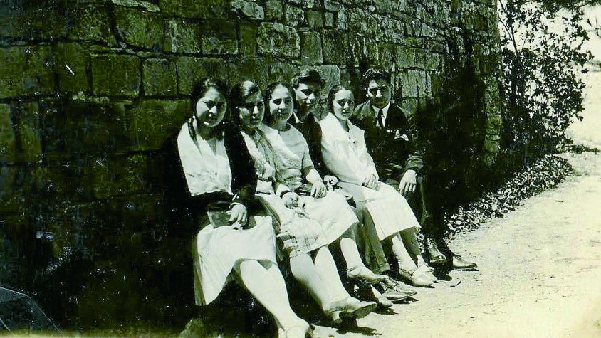 En Tomàs Pomés de jove, el quart enmig de les noies i un noi, al costat del mur on hi ha la Font dels Enamorats de Sant Eloi, 1920
