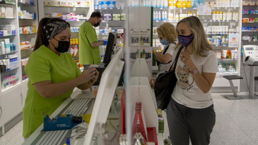 Treballadors i clients d'una farmàcia amb mascareta, que deixarà de ser obligatòria en aquests espais