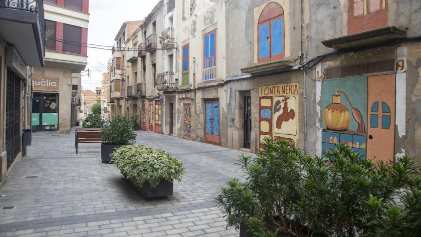 El carrer Urgell, amb la botiga acabada de tancar (esquerra) i els murals dels comerços antics (dreta)