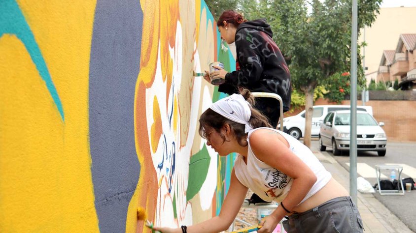 Les artistes Didi i Ariita pintant el seu mural que fa homenatge a les migdiades d'estiu