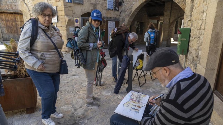 Un dels participants dibuixant mentre dos turistes l'observen