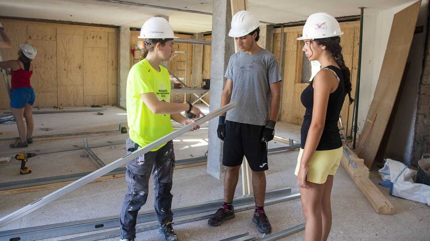 Una estudiant d’Arquitectura dona indicacions a dos joves del camp de treball