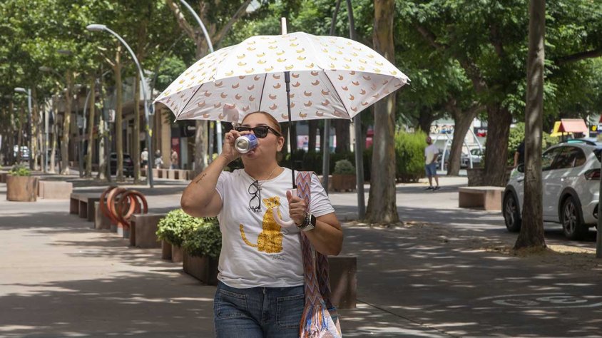 Una dona protegint-se del sol amb un paraigua mentre beu una beguda fresca
